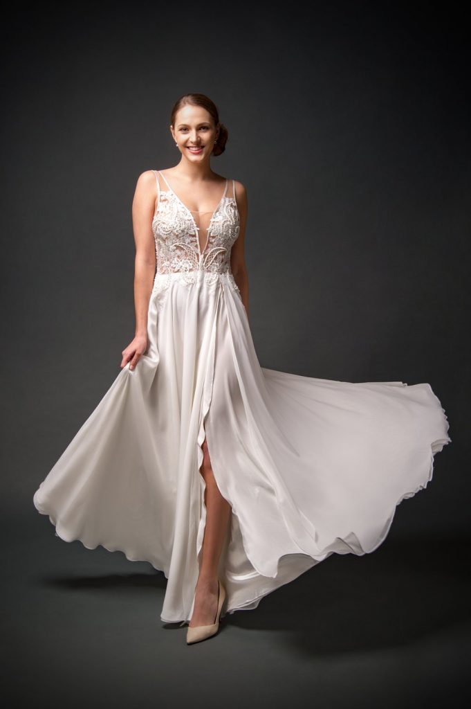 A bride wearing a flowing chiffon and lace wedding dress with a deep-V neckline, hand-beaded lace bodice, and a slit skirt, perfect for a beach-y or boho style.