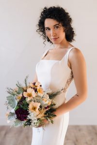 Square neck trumpet wedding dress holding a bouquet with peach flowers. Modern wedding dress