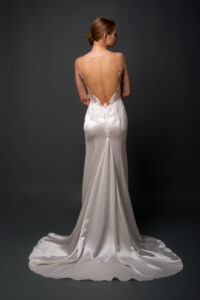 Bride wearing a satin backless gown with delicate lace detail and a flowing train, standing with her back to the camera.