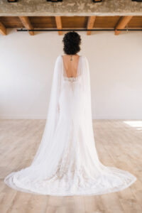 Back of bride wearing a square neck trumpet wedding dress with a lace train and tulle cape
