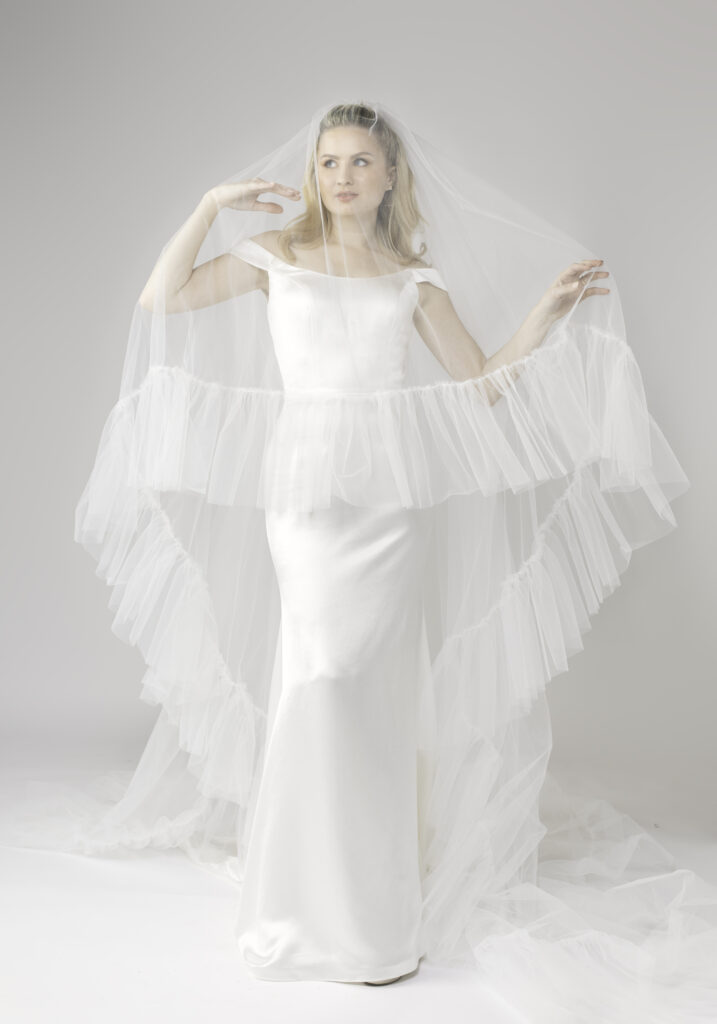 Elegant bride in an off-the-shoulder gown with a long ruffle veil, showcasing a soft and romantic bridal look.