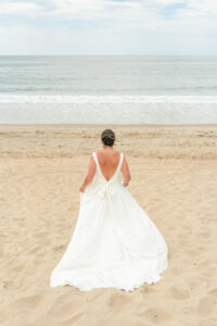 bride running away on beach in ivory crepe dress with low back and long bow