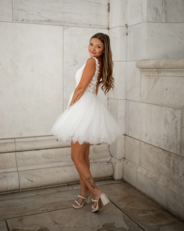 Side profile of a woman in a lace and tulle short wedding dress, highlighting the floral lace straps and flowy tulle skirt.